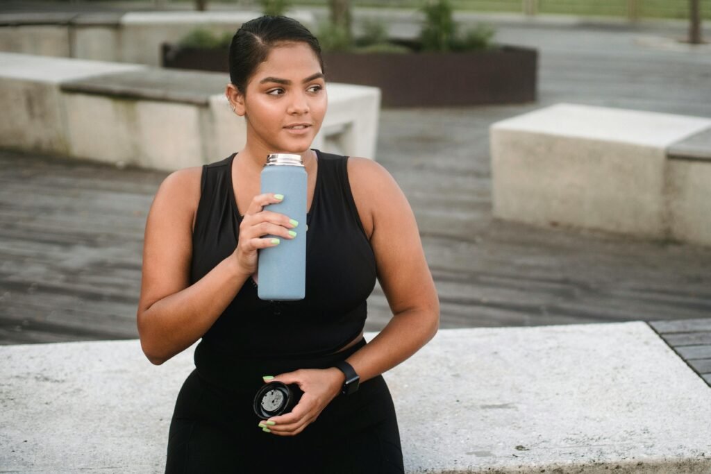 Fit woman in activewear taking a break outdoors, holding a tumbler for hydration.